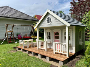 a2 disain täispuidust laste mängumaja Rannamaja  valgete lillekastide, puust terrassi ja  roosa uksega tagaaias